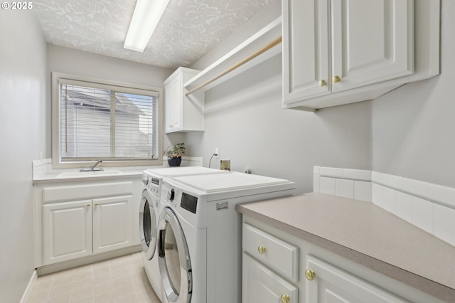 clothes washing area with a textured ceiling, washing machine and dryer, cabinets, and sink