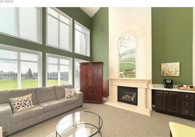 living area with a large fireplace, visible vents, a towering ceiling, and light carpet