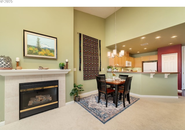 dining space featuring an inviting chandelier, light colored carpet, baseboards, and a tile fireplace