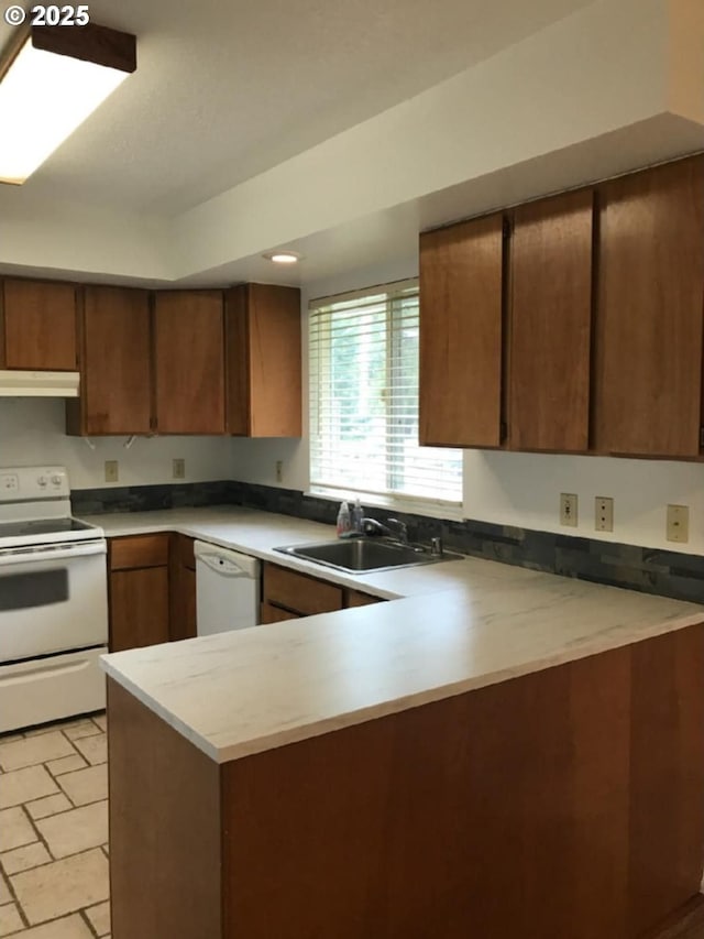 kitchen with a sink, white appliances, light countertops, a peninsula, and under cabinet range hood