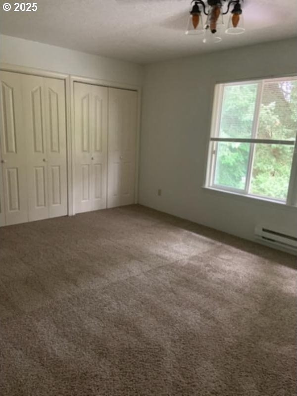 unfurnished bedroom featuring baseboard heating, carpet, two closets, and a ceiling fan