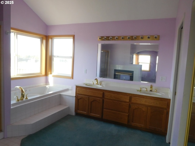 bathroom featuring a relaxing tiled tub, lofted ceiling, vanity, and a tile fireplace