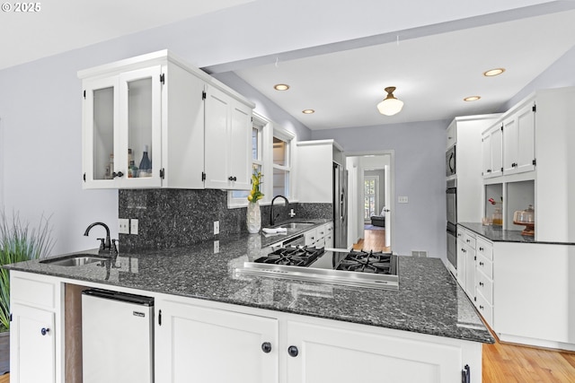 5707 SW Menefee Dr, Portland, OR 97239 - kitchen featuring appliances with stainless steel finishes, dark stone countertops, white cabinets, a peninsula, and recessed lighting