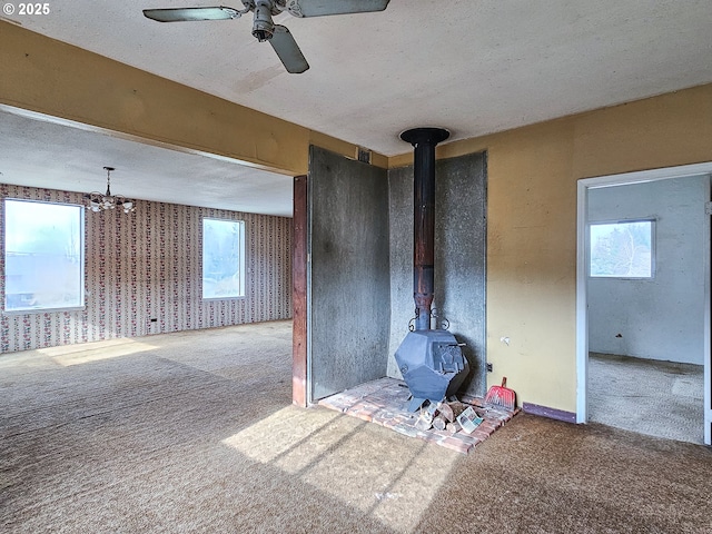 unfurnished living room featuring a textured ceiling, carpet floors, ceiling fan, and a wood stove