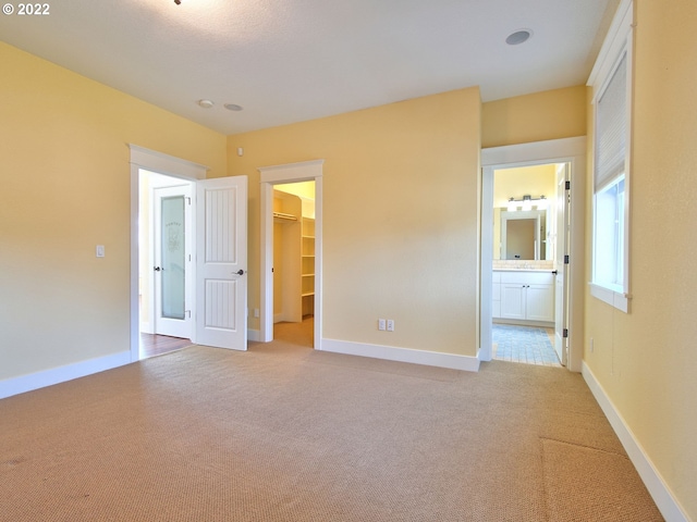 unfurnished bedroom with a spacious closet, ensuite bath, light colored carpet, and a closet