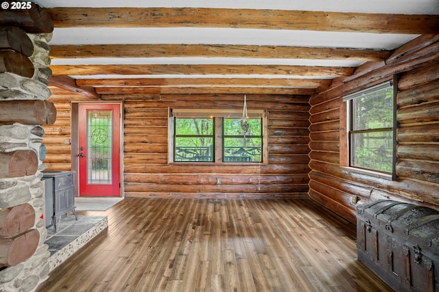 unfurnished living room featuring wood-type flooring, a wood stove, a wealth of natural light, and beamed ceiling
