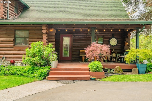 entrance to property featuring a porch, log siding, and a shingled roof