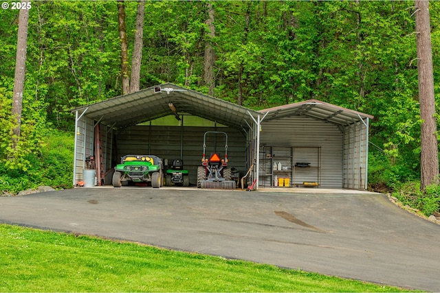 view of car parking with a view of trees, a detached carport, and aphalt driveway