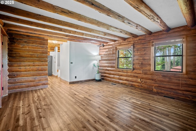 interior space with visible vents, rustic walls, wood finished floors, beamed ceiling, and baseboards