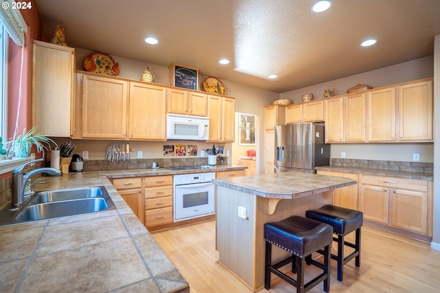 kitchen with white appliances, light brown cabinets, a sink, a kitchen island, and recessed lighting