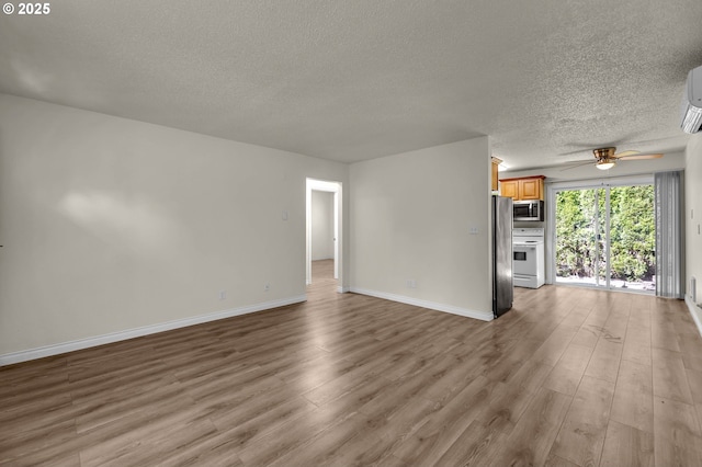 2117 Kauffman Ave, Vancouver, WA 98660 - unfurnished living room featuring a textured ceiling, wood finished floors, a ceiling fan, baseboards, and a wall mounted air conditioner