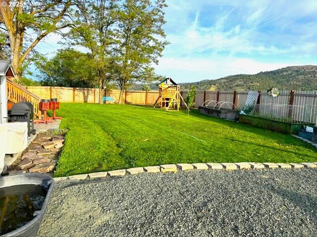 view of yard with a fenced backyard, a playground, and a mountain view