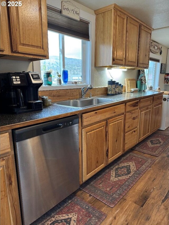 kitchen with stainless steel dishwasher, brown cabinetry, dark countertops, a sink, and dark wood finished floors