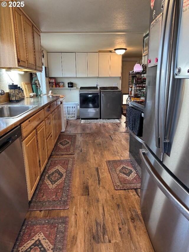 kitchen featuring dark wood-type flooring, a sink, appliances with stainless steel finishes, and washer and dryer