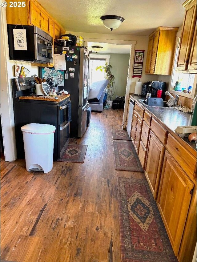 kitchen featuring brown cabinets, appliances with stainless steel finishes, a sink, and dark wood-type flooring