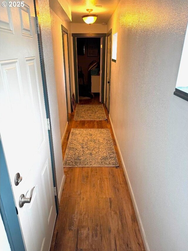 corridor with baseboards, a textured wall, and wood finished floors