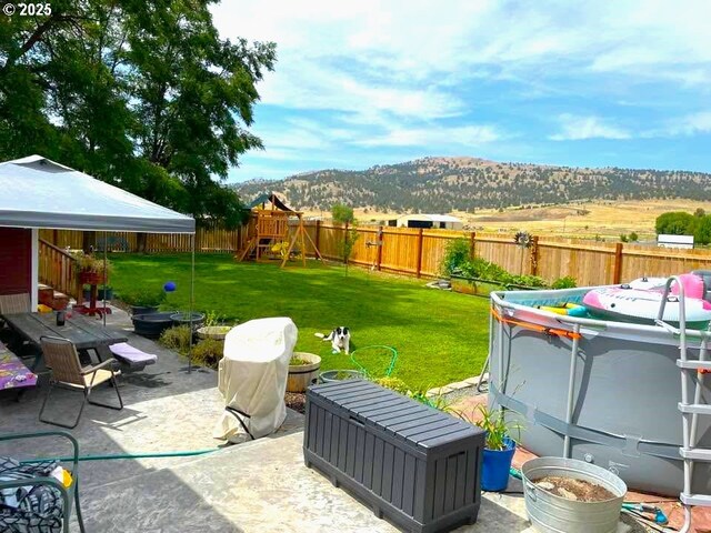 view of yard featuring a fenced backyard, a mountain view, a playground, and a patio area