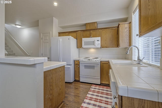 kitchen featuring tile countertops, white appliances, a sink, a wealth of natural light, and brown cabinetry