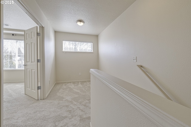 corridor with light carpet, a textured ceiling, visible vents, and baseboards