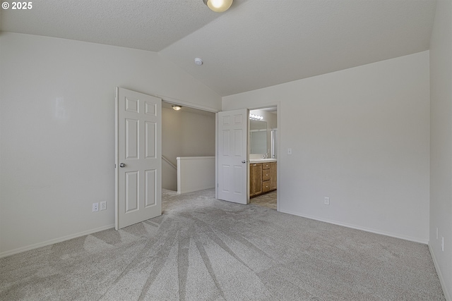 unfurnished bedroom with light colored carpet, lofted ceiling, ensuite bath, a textured ceiling, and a sink