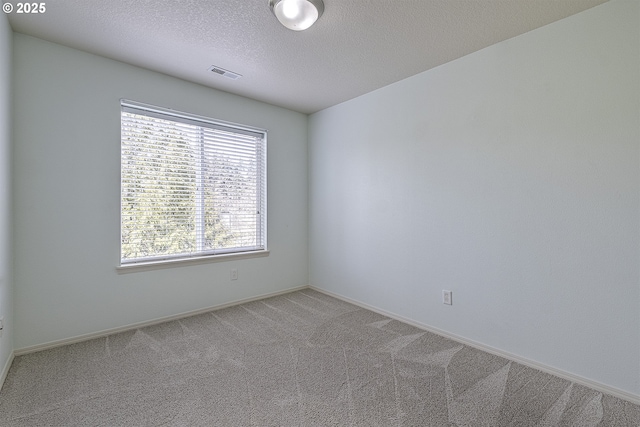 unfurnished room with a textured ceiling, carpet, visible vents, and baseboards