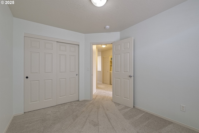 unfurnished bedroom with light carpet, a closet, a textured ceiling, and baseboards