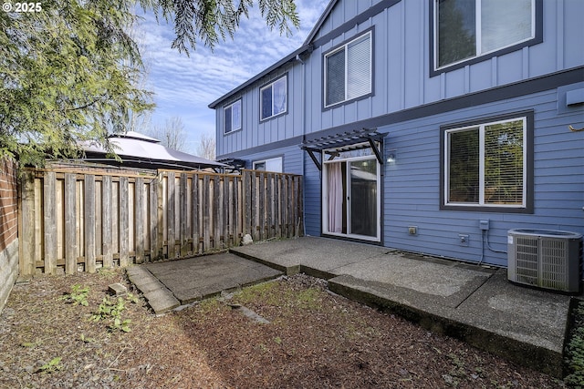 back of house with board and batten siding, a patio area, central AC, a pergola, and a fenced backyard