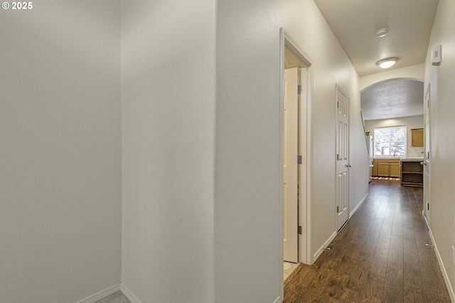 corridor with a textured ceiling, baseboards, arched walkways, and dark wood-type flooring