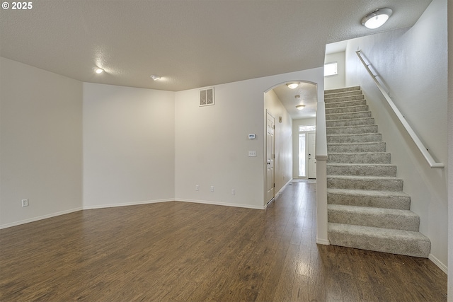 interior space featuring visible vents, arched walkways, stairway, dark wood-style flooring, and a textured ceiling