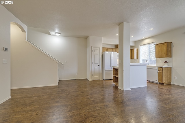 unfurnished living room featuring dark wood-style floors, arched walkways, a textured ceiling, and baseboards