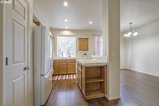 kitchen featuring dark wood-style floors, open shelves, tile counters, brown cabinetry, and freestanding refrigerator