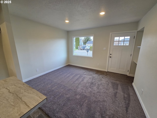 foyer entrance with a textured ceiling and dark colored carpet