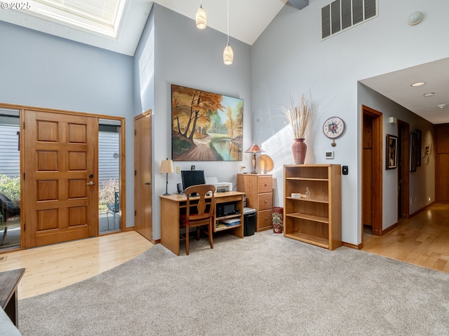 carpeted entrance foyer with visible vents, wood finished floors, high vaulted ceiling, and a skylight