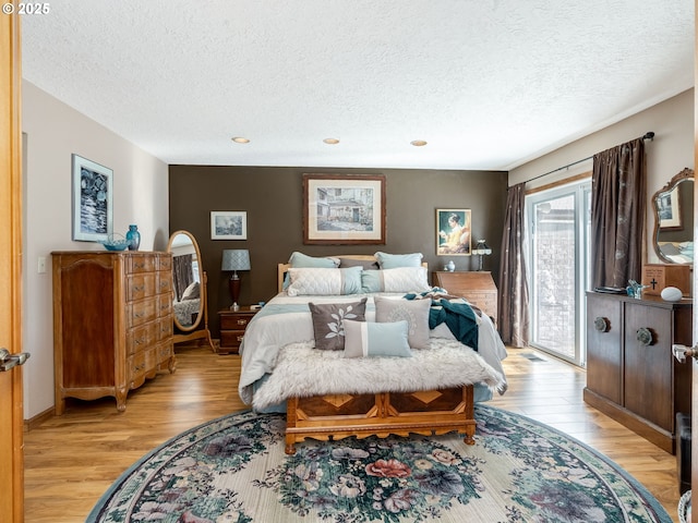 bedroom with access to exterior, a textured ceiling, and light wood-type flooring