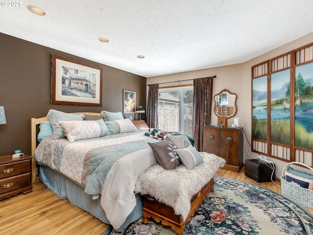 bedroom with access to exterior, light wood-style flooring, and a textured ceiling