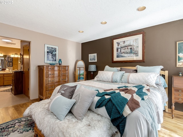 bedroom featuring light wood-style flooring, a textured ceiling, ensuite bathroom, and baseboards