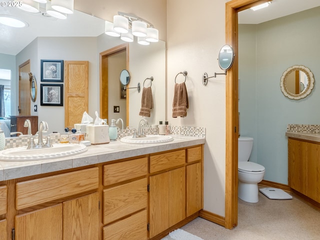 bathroom with a sink, baseboards, toilet, and double vanity