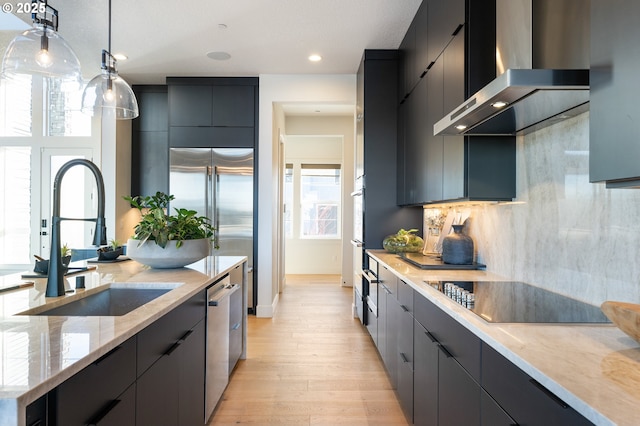 kitchen with pendant lighting, backsplash, wall chimney range hood, sink, and stainless steel appliances