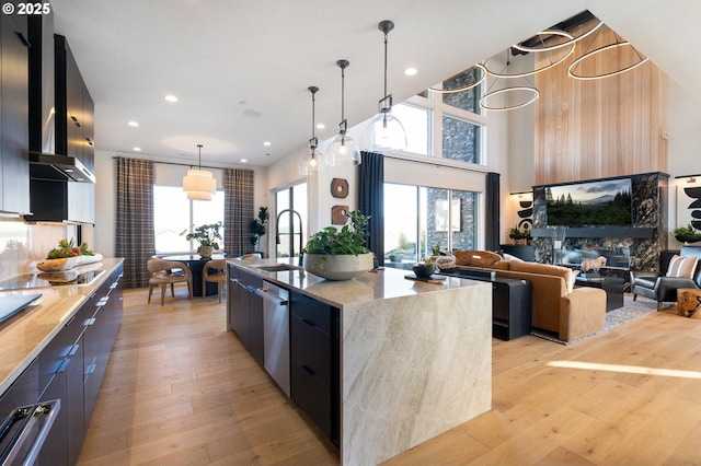 kitchen featuring sink, a high end fireplace, an island with sink, pendant lighting, and light wood-type flooring