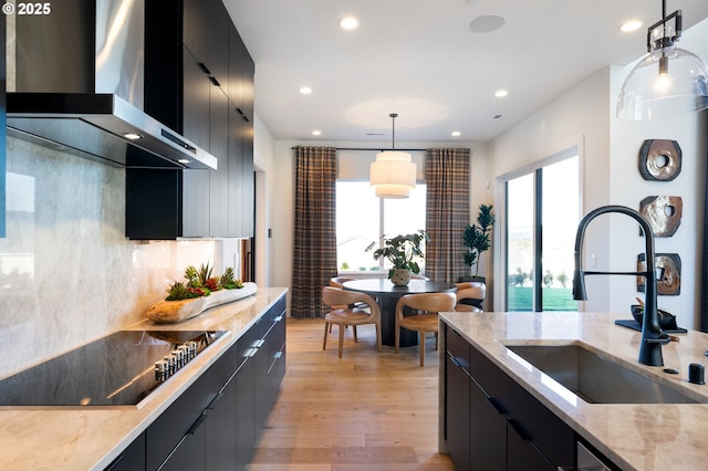 kitchen featuring sink, wall chimney range hood, pendant lighting, black electric stovetop, and light wood-type flooring