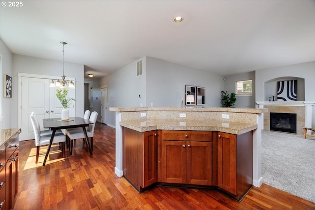 kitchen with a notable chandelier, tile counters, brown cabinetry, dark wood-type flooring, and visible vents