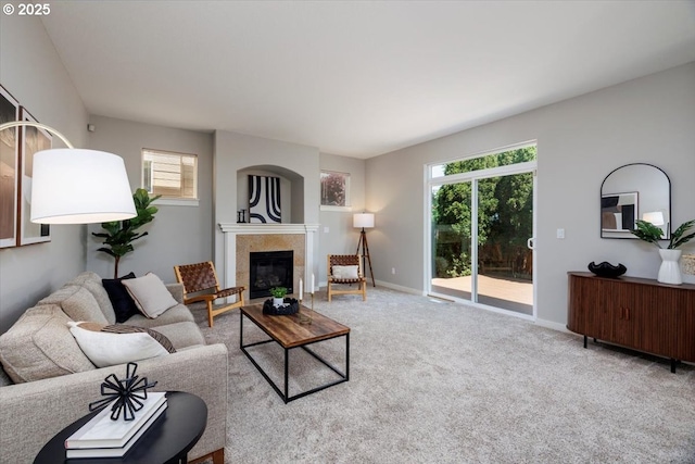 living room with a tiled fireplace, carpet flooring, baseboards, and plenty of natural light