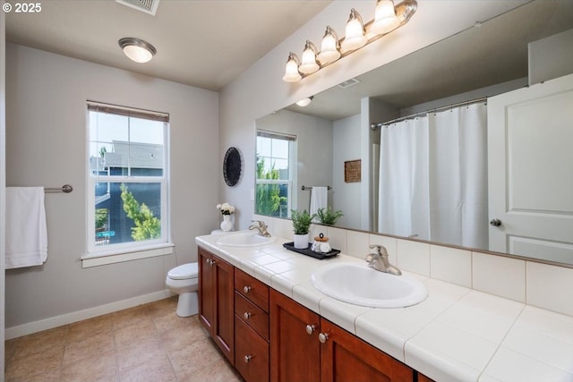 bathroom featuring toilet, double vanity, baseboards, and a sink