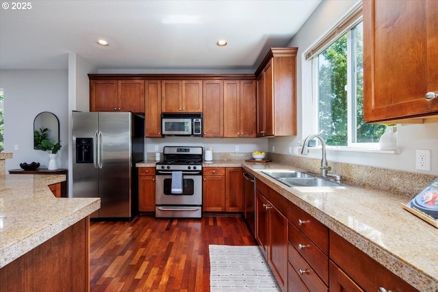 kitchen featuring appliances with stainless steel finishes, a sink, dark wood finished floors, brown cabinetry, and recessed lighting