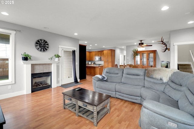 living room featuring ceiling fan, a tiled fireplace, and light wood-type flooring