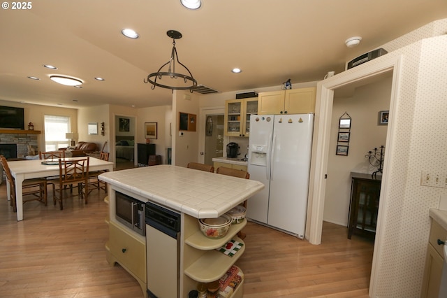 kitchen featuring hanging light fixtures, white refrigerator with ice dispenser, light hardwood / wood-style floors, a stone fireplace, and tile countertops