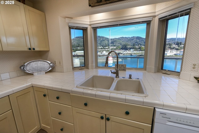 kitchen featuring sink, tile countertops, a water and mountain view, white dishwasher, and cream cabinetry