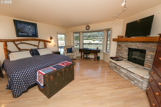 bedroom with a fireplace, track lighting, and light hardwood / wood-style floors