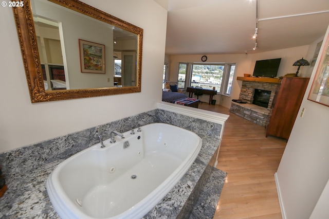 bathroom featuring a relaxing tiled tub, wood-type flooring, and a fireplace