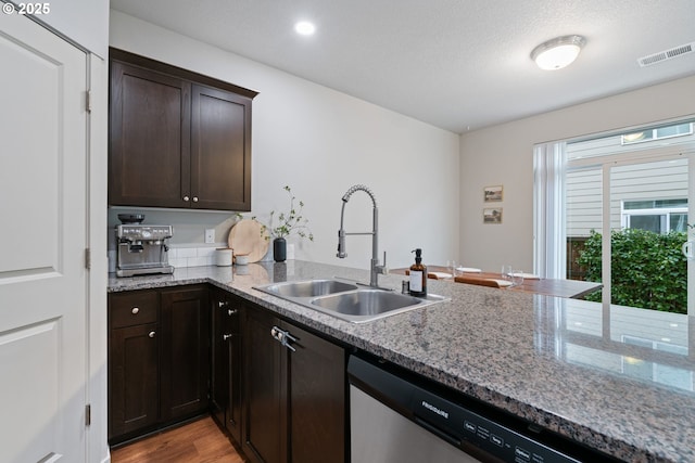 kitchen featuring sink, stainless steel dishwasher, light hardwood / wood-style floors, light stone counters, and dark brown cabinetry